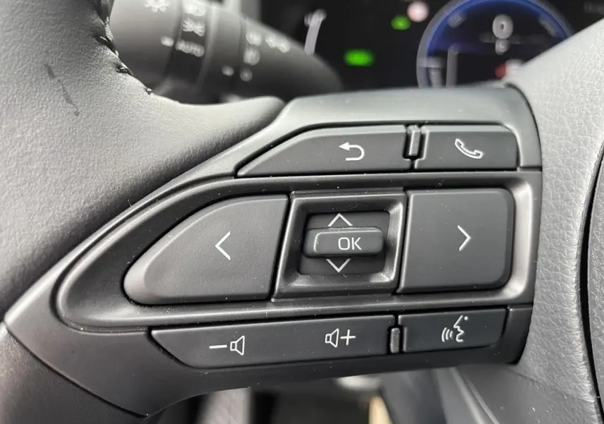 Gros plan sur les commandes multifonctions noires au volant côté gauche de la Toyota Yaris Cross hybride 2026.