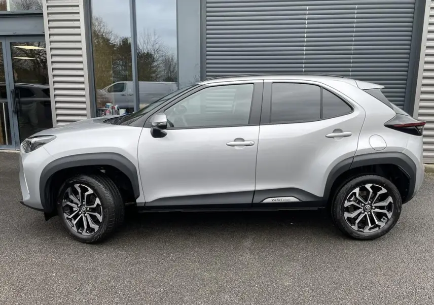 Profil droit d'un Toyota Yaris Cross gris clair avec jantes alliage noires et logo Yaris Cross sur bas de caisse.