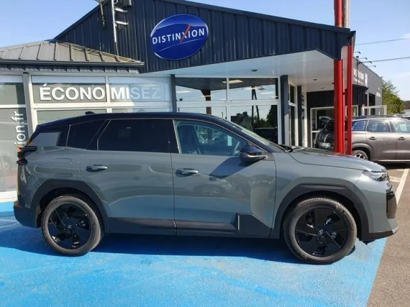 Vue de profil côté gauche d'un Citroën C5 Aircross 2026 vert Astoria avec jantes noires, stationné devant un concessionnaire.