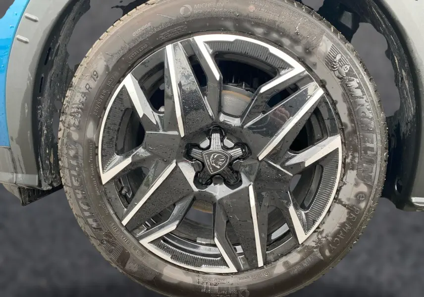 Gros plan sur la jante alu noire et argentée d’un Peugeot 3008 bleu, montrant le logo lion central.