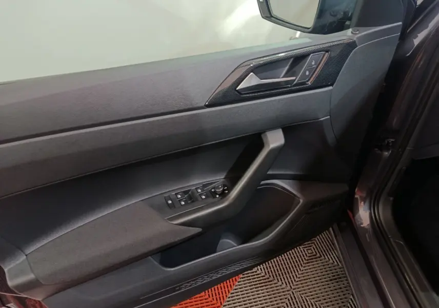 Vue intérieure côté gauche de la porte avant gris foncé de la Volkswagen Polo 2025 avec commandes électriques et poignée intégrée.