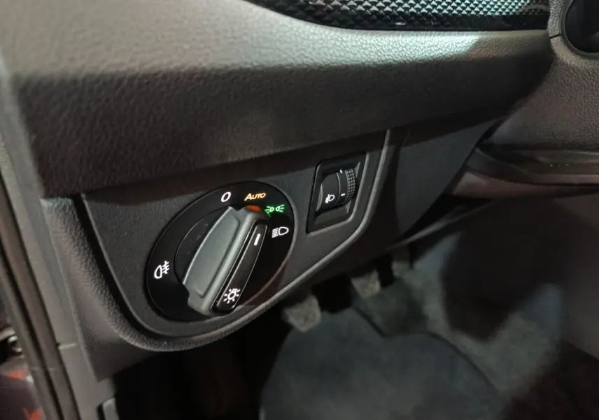 Gros plan sur le bouton de commande des phares et réglage d’intensité dans l’habitacle noir d’une Volkswagen Polo 2025 gris foncé.