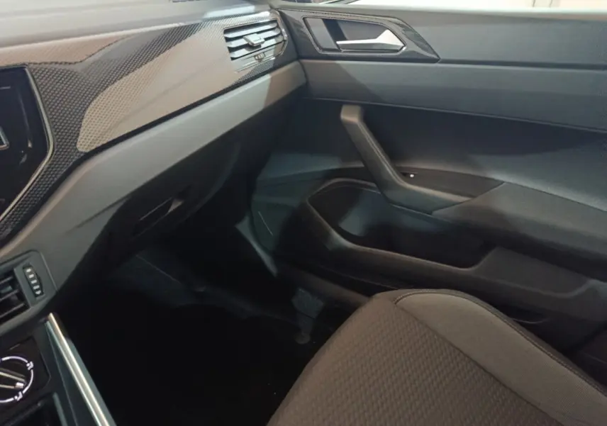 Vue intérieure côté passager de la Volkswagen Polo 2025 gris foncé, montrant la planche de bord et la porte avec finition carbone.