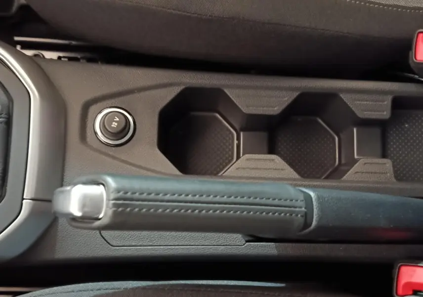 Vue rapprochée de la console centrale de la Volkswagen Polo gris foncé, avec frein à main manuel et prise 12V.