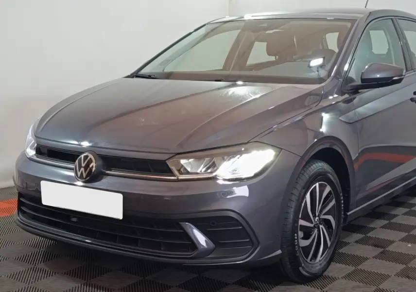 Volkswagen Polo gris foncé vue 3/4 avant droit avec phares allumés et jantes alliage distinctives.
