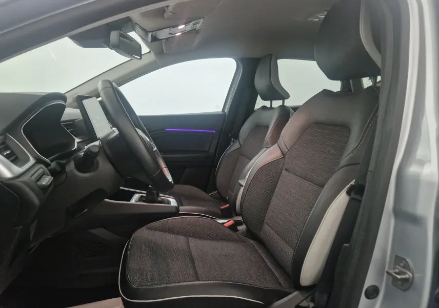 Vue intérieure côté conducteur du Renault Captur 2024, sièges tissu noir avec surpiqûres blanches et éclairage d'ambiance violet.