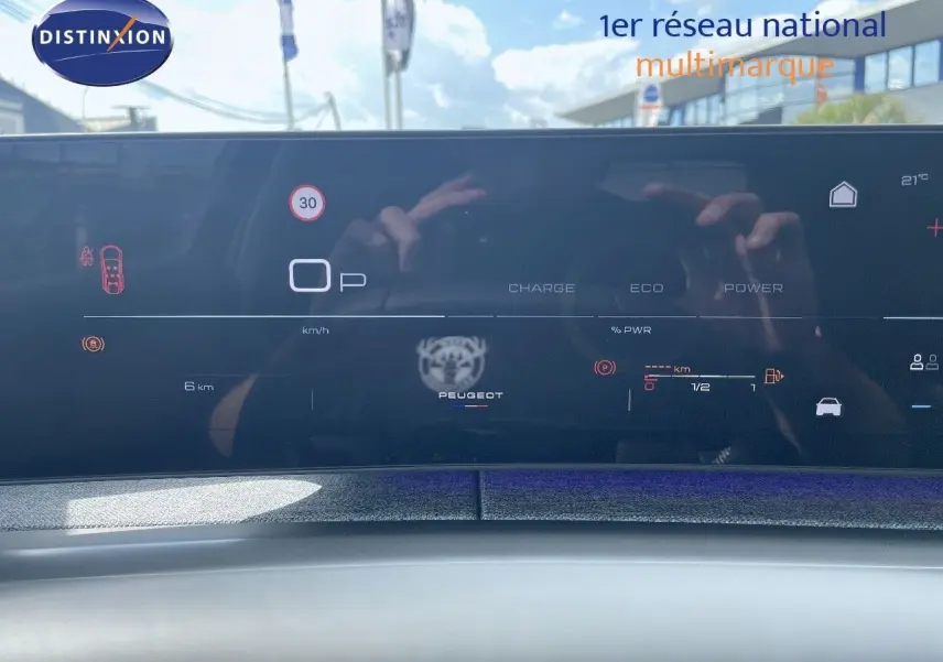 Tableau de bord numérique du Peugeot 5008 Hybrid 136ch GT 2025 affichant vitesse et autonomie, avec reflet extérieur.