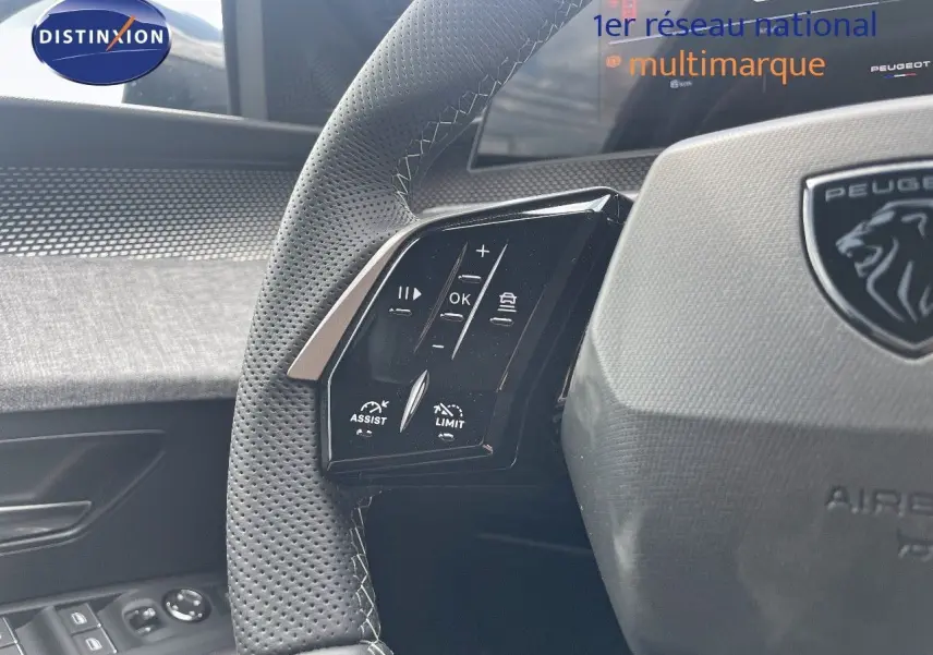 Gros plan sur le volant en cuir perforé noir du Peugeot 5008 Hybrid 2025 avec commandes intégrées et logo lion.