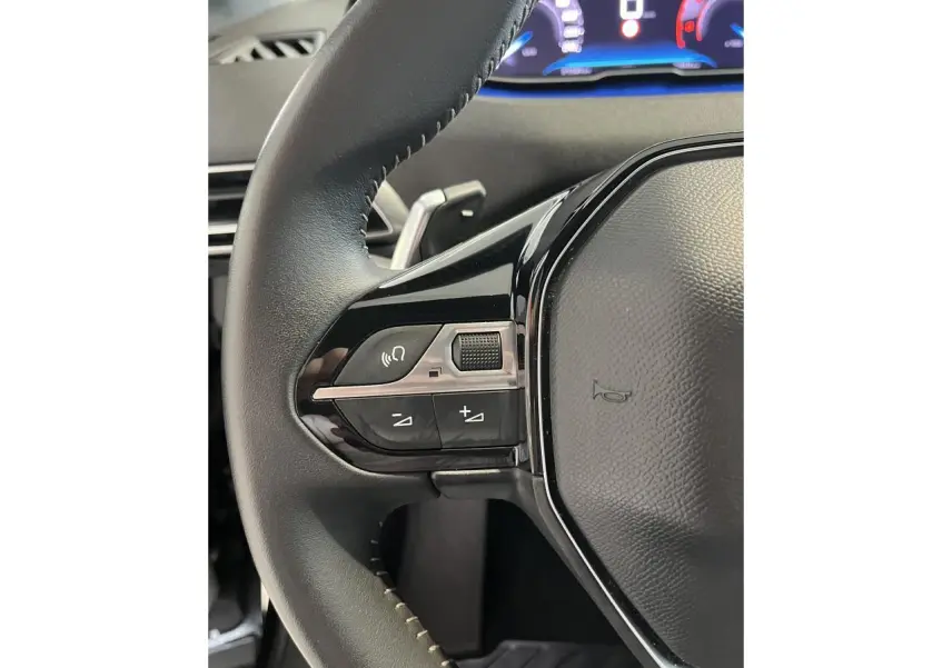 Gros plan sur le volant noir cuir du Peugeot 5008 2024 avec commandes intégrées et tableau de bord numérique lumineux.