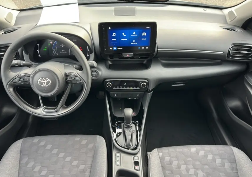 Intérieur de la Toyota Yaris 2025 hybride, vue frontale du tableau de bord avec écran tactile et levier de boîte automatique.