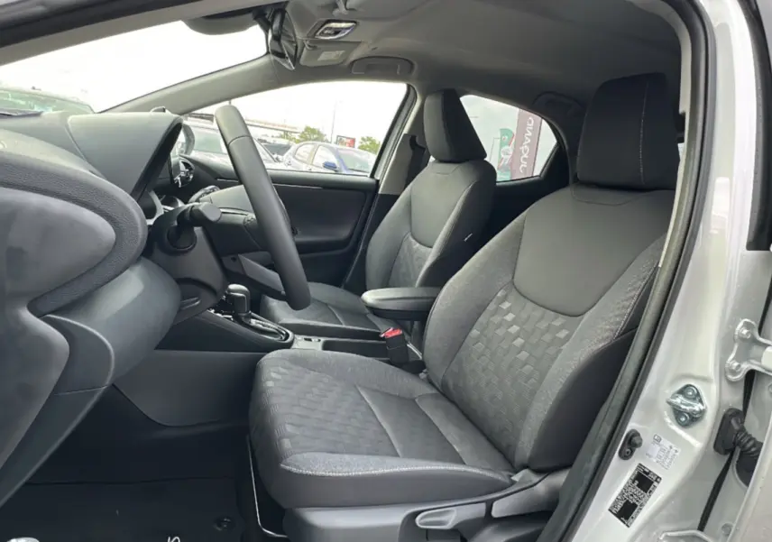 Vue intérieure côté conducteur de la Toyota Yaris 2025 blanc lunaire, sièges tissu gris avec motifs géométriques.