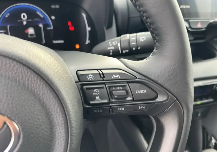 Gros plan sur le volant de la Toyota Yaris 2025 blanc lunaire, montrant les commandes de régulateur et d’aide à la conduite.
