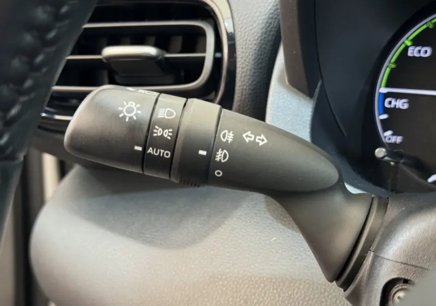Gros plan sur la commande des phares et clignotants à gauche du volant dans l’habitacle de la Toyota Yaris hybride blanche.