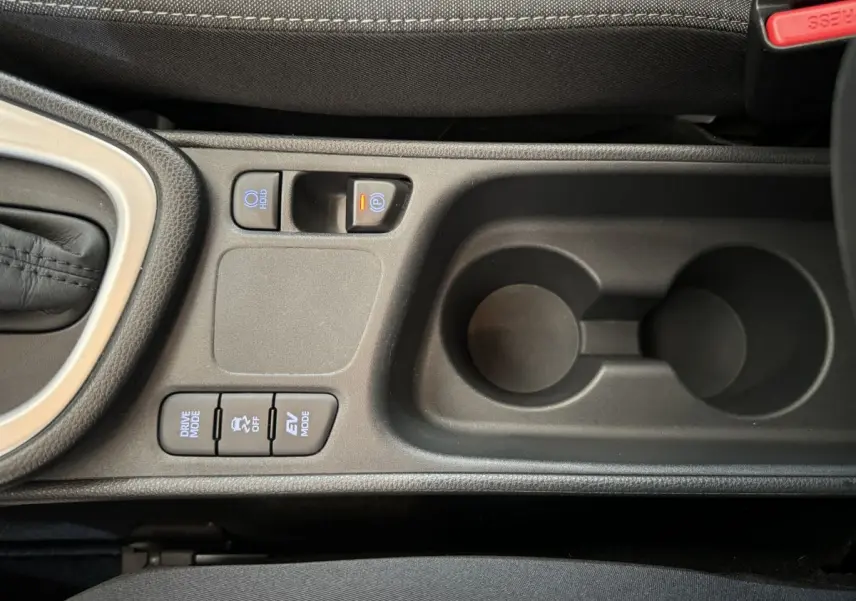 Vue rapprochée de la console centrale noire de la Toyota Yaris hybride 2022 avec boutons de modes de conduite et frein à main électrique.