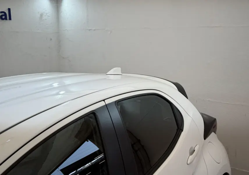 Vue latérale droite arrière d'une Toyota Yaris hybride blanche avec antenne requin sur le toit.