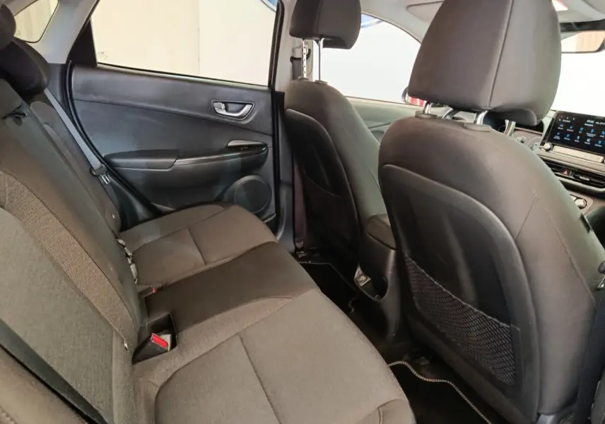 Vue intérieure arrière du Hyundai Kona électrique 2023, sièges tissu gris et dossier avant en cuir noir.