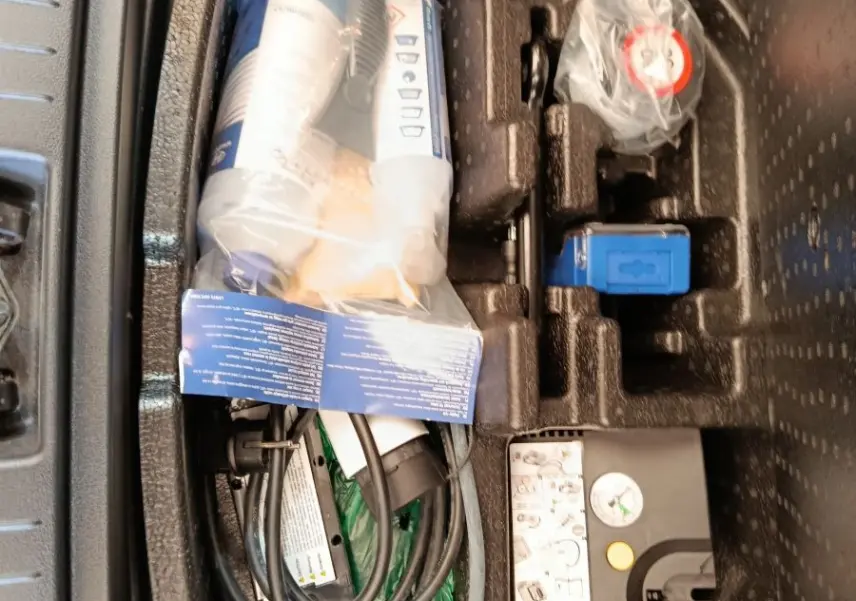 Rangement sous plancher de coffre avec câble de charge et kit de réparation sur Hyundai Kona électrique noir, vue de dessus.