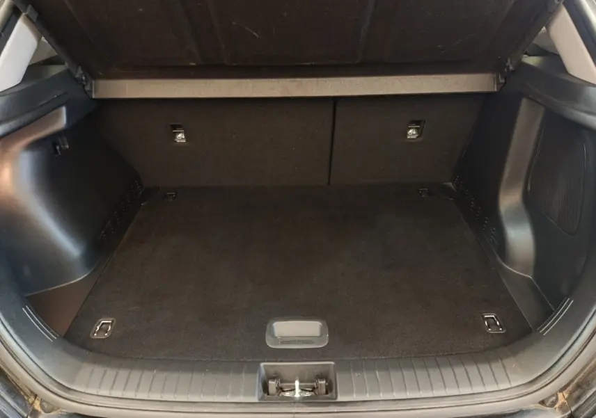 Coffre ouvert vu de l'arrière d'un Hyundai Kona électrique noir, espace de chargement vide et tapis noir.