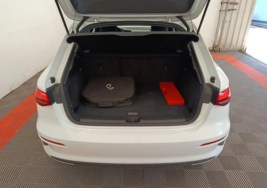 Vue arrière d'un Audi A3 blanc 2022 avec coffre ouvert montrant un sac de charge et une trousse rouge à l'intérieur.