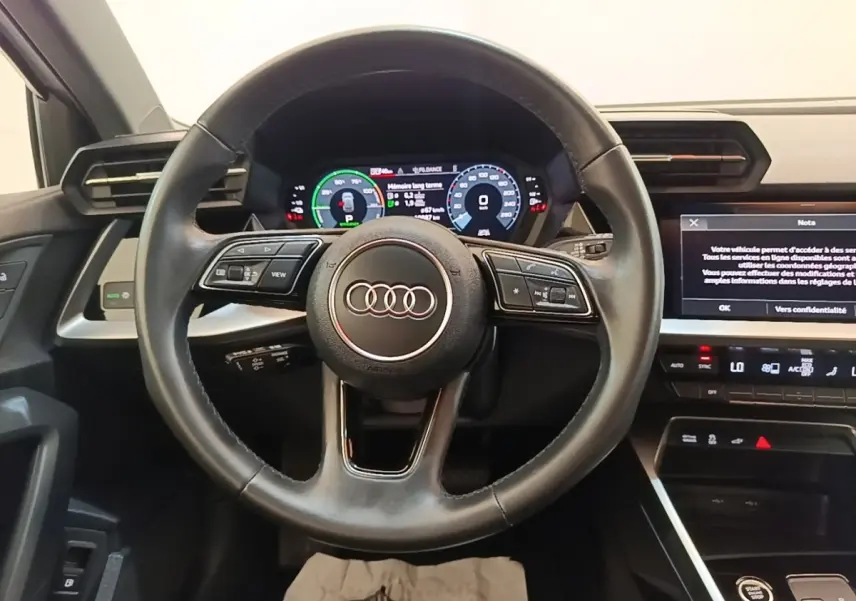 Vue centrée sur le volant cuir noir et le tableau de bord digital d'une Audi A3 40 TFSI e blanche de 2022.