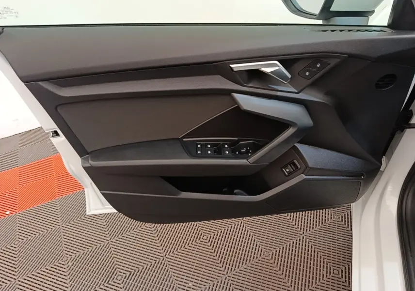 Vue intérieure de la porte avant gauche blanche d'Audi A3 40 TFSI e 2022 avec commandes électriques et poignée angulaire.