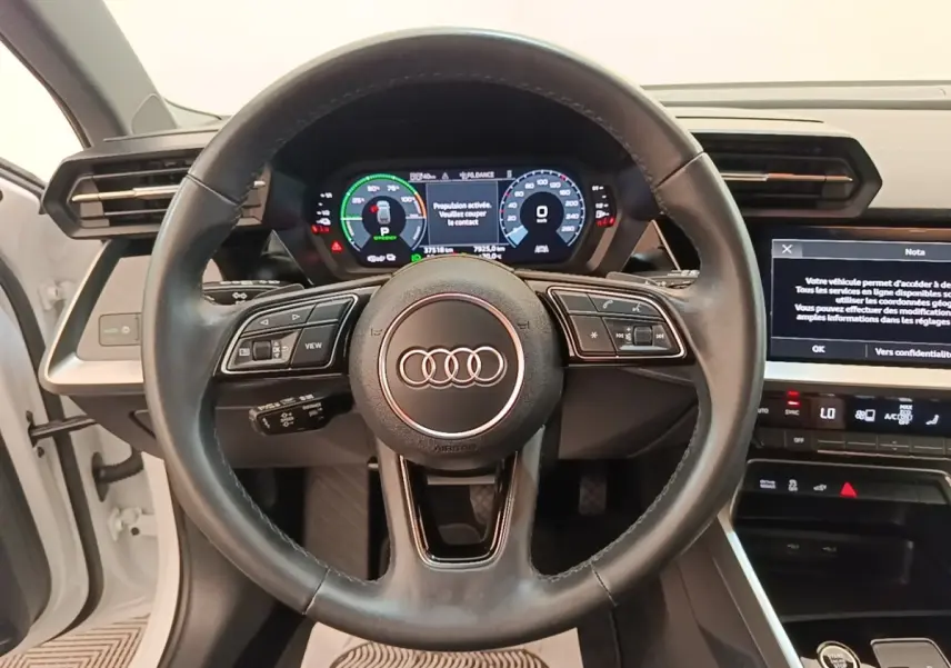 Vue centrée sur le volant cuir noir et le tableau de bord digital d'une Audi A3 blanche hybride rechargeable 2022.