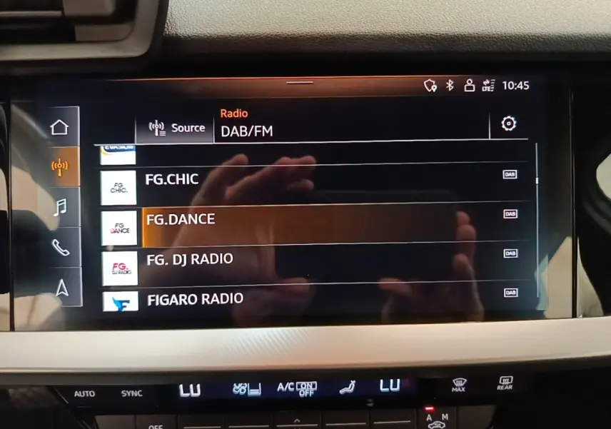 Écran tactile central de l'Audi A3 blanc, affichant les stations radio DAB/FM en intérieur.