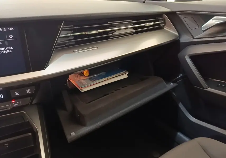 Intérieur Audi A3 40 TFSI e 2022, vue côté passager sur boîte à gants ouverte avec documents et tableau de bord noir et beige.