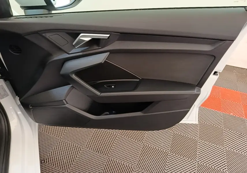 Vue intérieure côté gauche de la porte avant blanche d'une Audi A3 40 TFSI e avec garniture noire et poignée argentée.