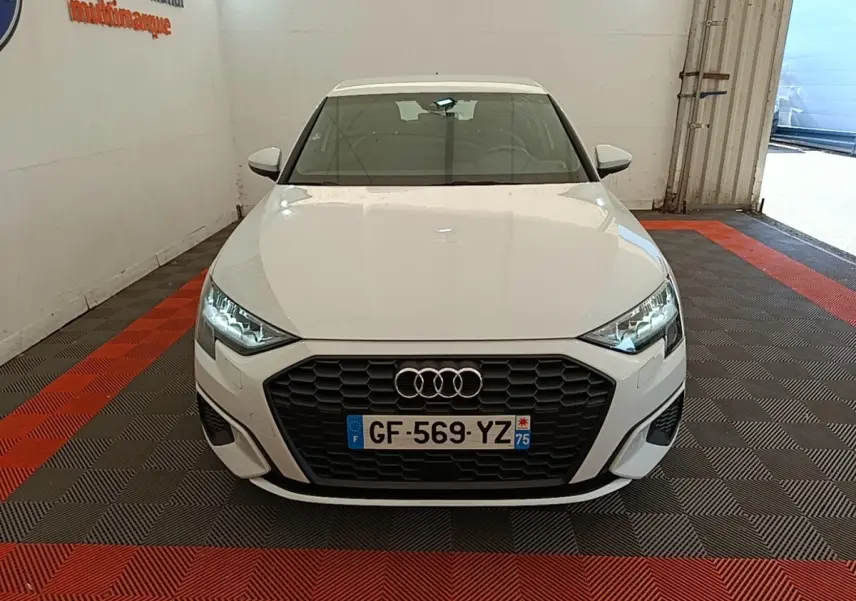 Audi A3 blanc vue de face dans un garage, avec calandre noire et phares LED allumés.