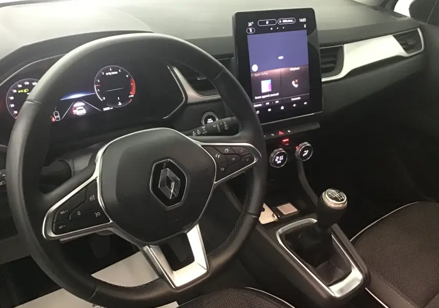 Vue intérieure du tableau de bord et volant Renault Captur blanc nacré/ noir, avec écran tactile vertical et levier de vitesse manuel.