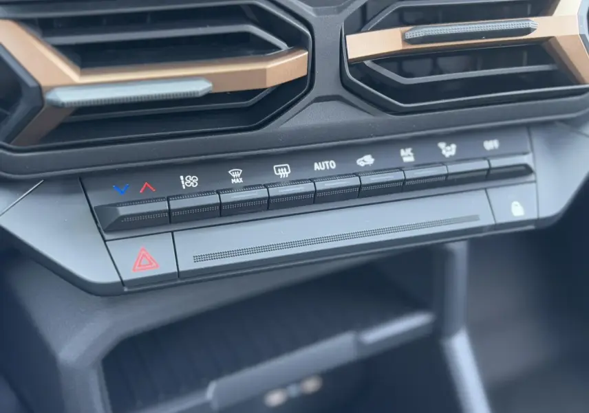 Gros plan sur la console centrale du Dacia Duster 2025, montrant les commandes de climatisation et les aérateurs avec inserts cuivrés.