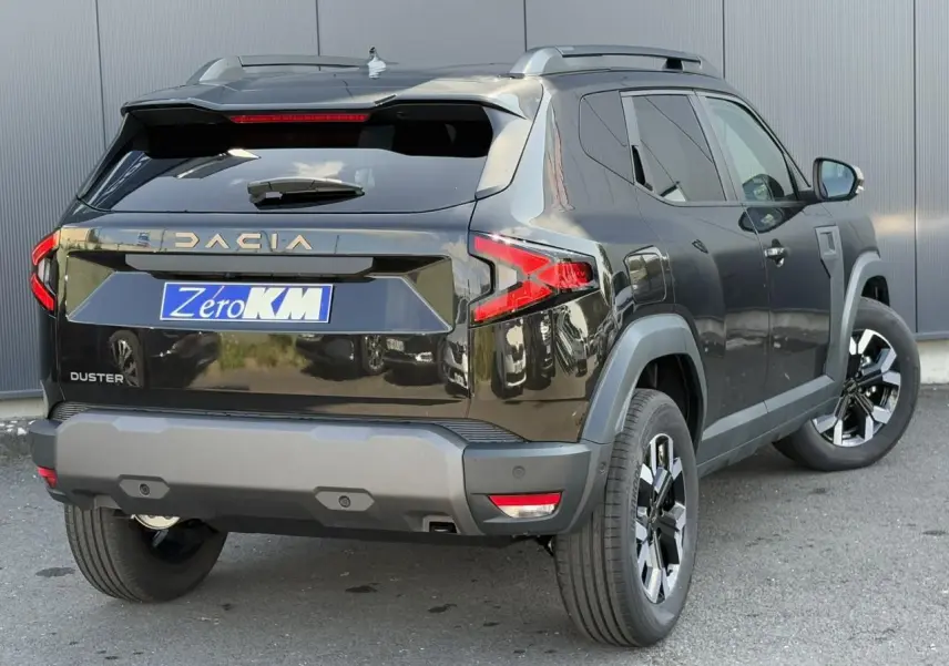 Vue 3/4 arrière droite du Dacia Duster noir nacré avec jantes alliage et barres de toit visibles.