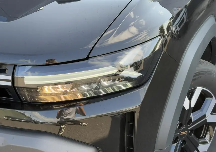 Gros plan sur le phare avant droit et la jante alliage 17" du Dacia Duster noir nacré 2025.