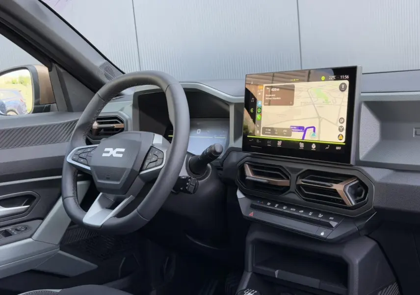 Vue intérieure côté conducteur du tableau de bord du Dacia Duster 2025 avec écran tactile GPS et volant multifonctions.