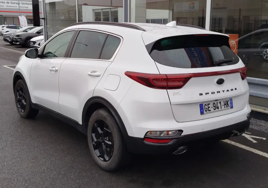 Vue 3/4 arrière droite d'un KIA Sportage blanc 2022 avec jantes noires et feux arrière allongés.