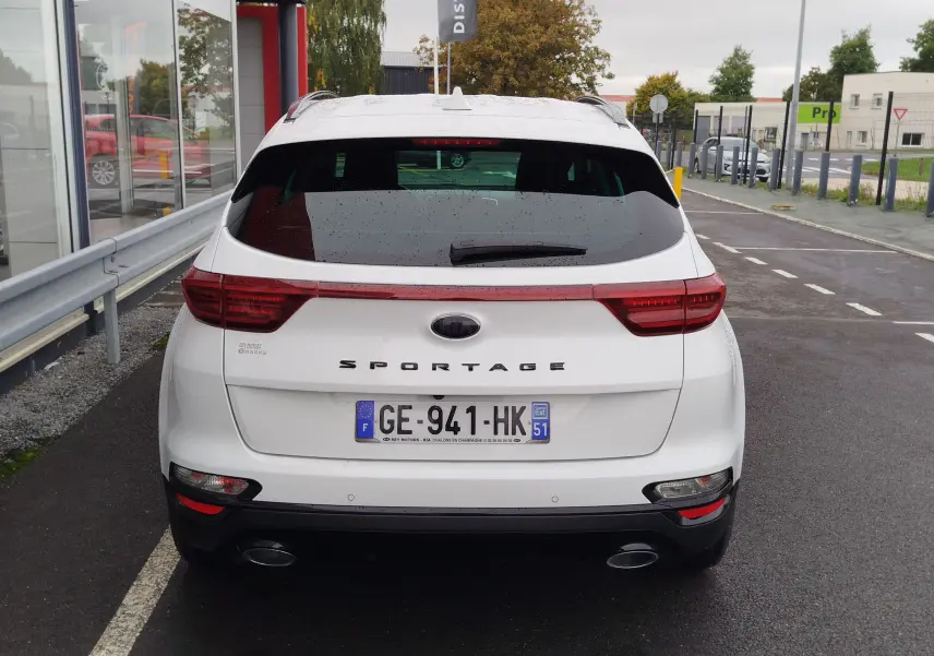Vue arrière d'un KIA Sportage blanc 2022 avec feux LED et double sortie d'échappement sur parking humide.