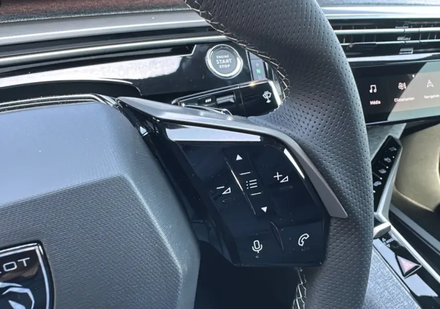 Gros plan sur le volant perforé du Peugeot 3008 Hybrid 2025 avec commandes intégrées et bouton start/stop visible.
