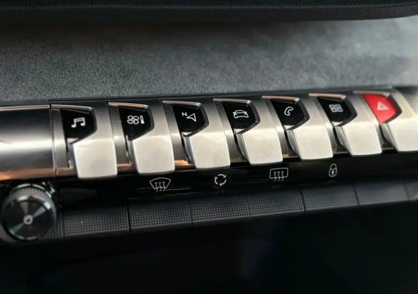 Gros plan sur les commandes en métal brossé du tableau de bord du Peugeot 3008 GT 2023, avec touches fonctionnelles noires.