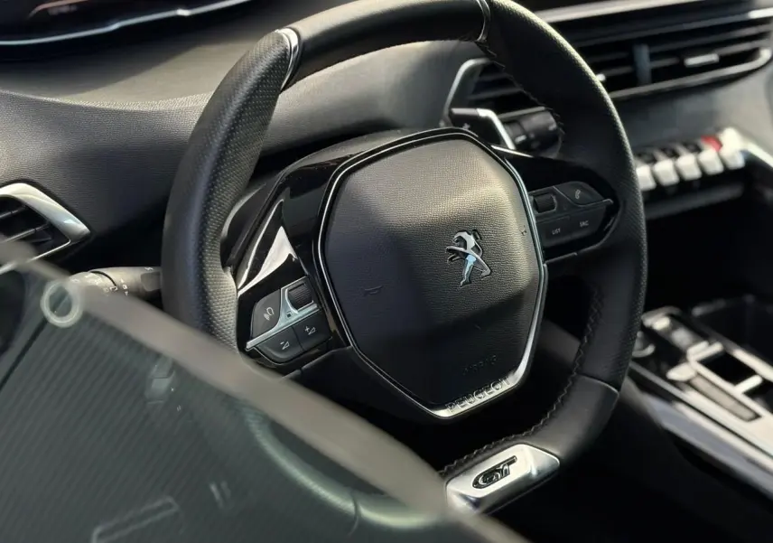 Gros plan sur le volant cuir perforé noir avec logo Peugeot et badge GT dans l’habitacle du 3008 2023.