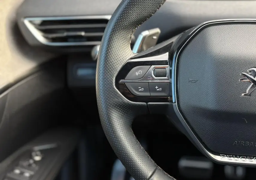 Gros plan sur le volant cuir perforé du Peugeot 3008 GT 2023, avec commandes intégrées et logo lion chromé.