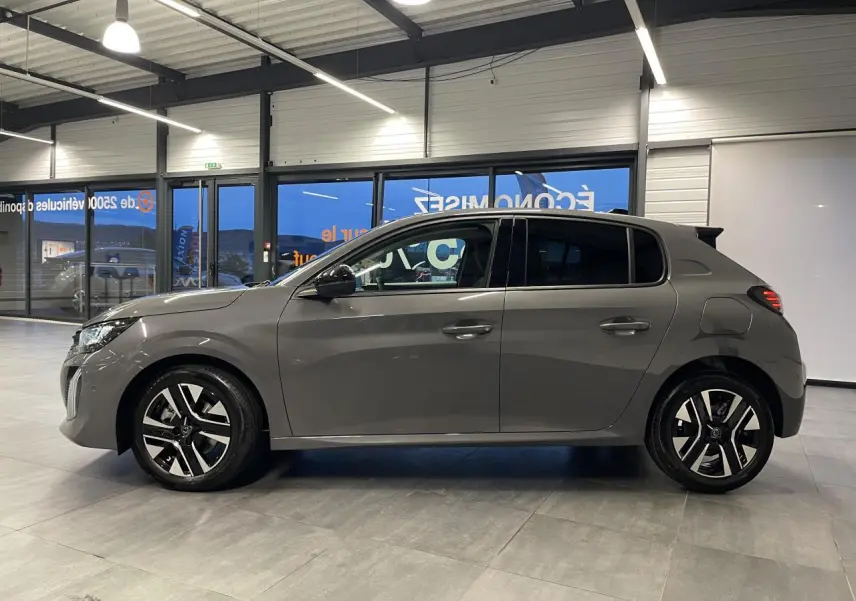 Vue de profil côté gauche d'une Peugeot 208 1.2i Hybrid gris selenium avec jantes alliage bi-tons en intérieur showroom.