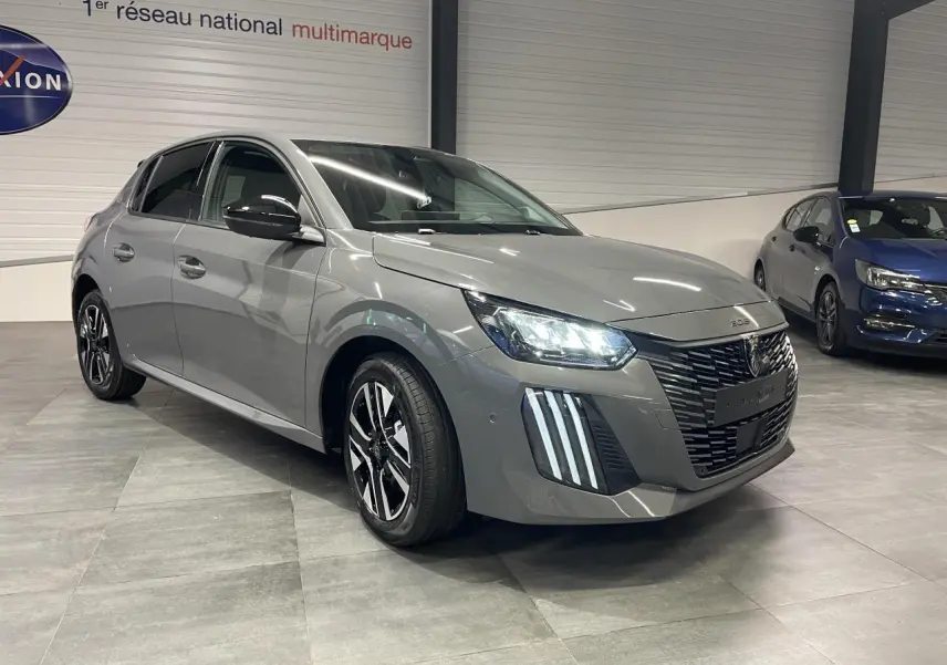 Peugeot 208 gris selenium en 3/4 avant droit avec calandre noire et feux LED allumés en intérieur showroom.