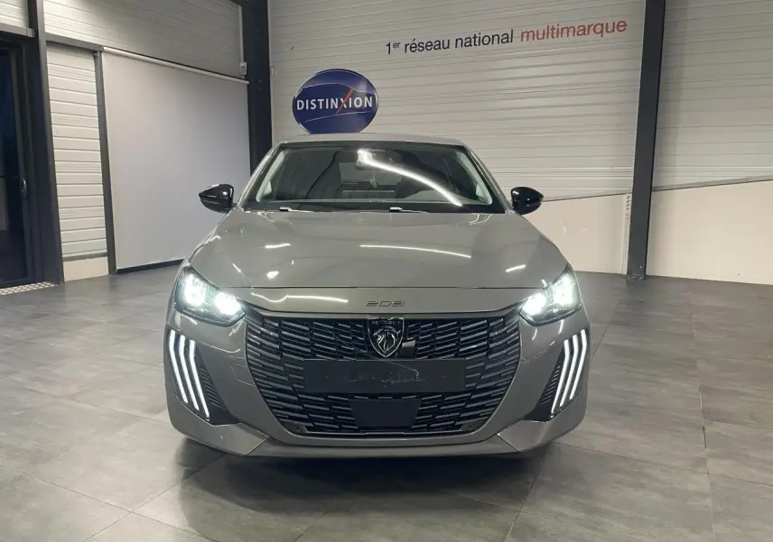 Vue avant d'une Peugeot 208 gris sélénium avec calandre noire et feux diurnes LED en forme de griffes allumés dans un showroom.