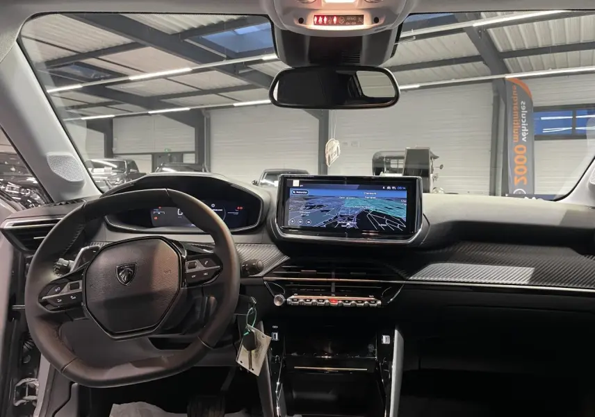 Vue intérieure avant du tableau de bord noir de la Peugeot 208 1.2i Hybrid avec écran tactile et volant compact cuir.