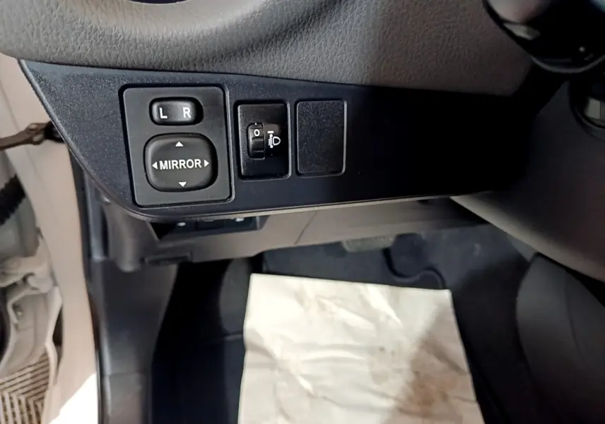 Vue rapprochée des commandes de réglage des rétroviseurs et des phares côté conducteur dans une Toyota Yaris blanche.