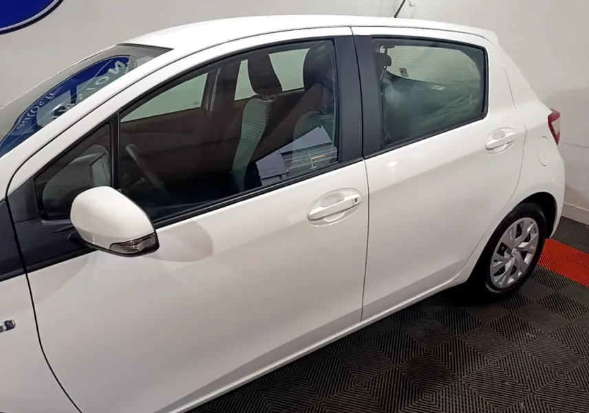 Vue de profil côté gauche d'une Toyota Yaris blanche 2019 hybride en intérieur, avec rétroviseur et poignées assortis.