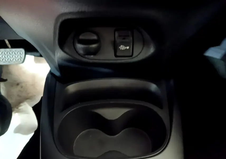 Gros plan sur le porte-gobelets central et commande d'ouverture du capot dans l'habitacle d'une Toyota Yaris blanche.