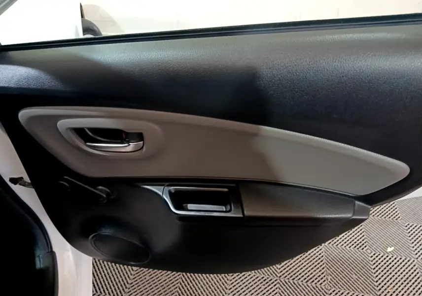 Vue intérieure du panneau de porte côté gauche de la Toyota Yaris blanche, avec poignée argentée et haut-parleur intégré.