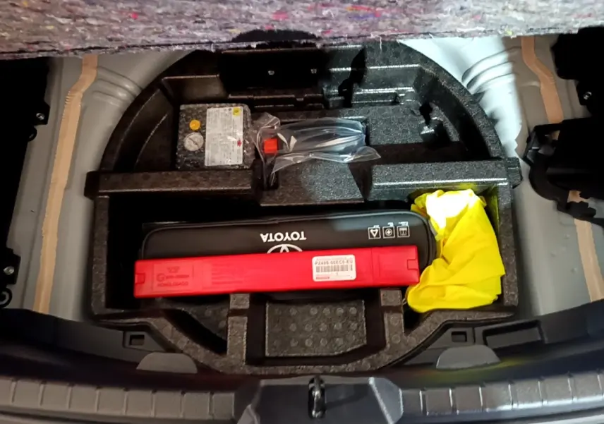 Vue plongeante sur le coffre ouvert d'une Toyota Yaris blanche, montrant le rangement d'accessoires et kit de sécurité.